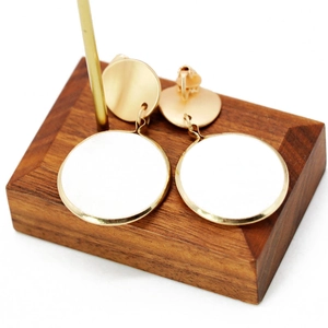 Close-up of elegant gold metal earrings with white circular finish on a wooden stand
