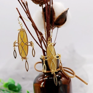 Detail view of gold earrings with yellow resin drops hanging on a dried branch
