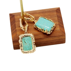 Macro detail of rectangle gold earrings with marble turquoise stone on wood stand