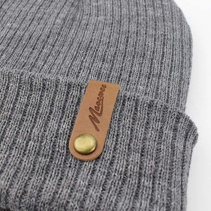 Grey ribbed knit beanie for men and women featuring a brown leather brand logo patch