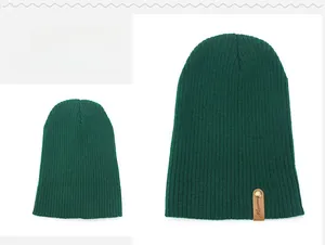 Macro detail of dark green ribbed knit beanie showing leather brand label and metal rivet