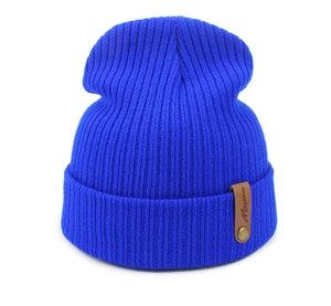 Detail view of bright blue ribbed knit beanie with brown leather patch and gold button