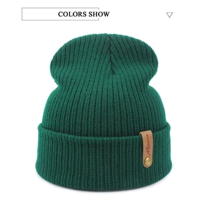 Close-up of dark green ribbed knit beanie with brown leather label and gold rivet detail