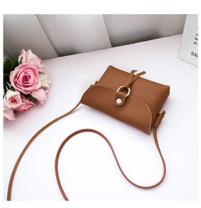 Close-up of caramel leather texture and golden ring buckle on a mini crossbody bag