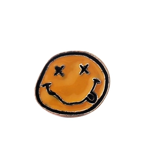 Gros plan sur un pin's rond en émail orange avec un visage souriant aux yeux en X et langue