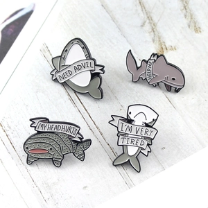 Cartoon shark enamel pins set with humorous ribbon text on white wood background