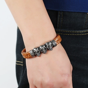 Brown braided leather bracelet with three metal skull charms worn by a male model