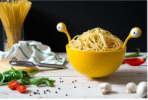 Close-up of yellow monster pasta strainer with googly eye handles in a kitchen setting