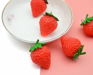 Detailed view of realistic red PVC strawberry charms with green leaves on a pink surface