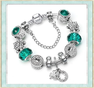 Detailed close-up of silver charm bracelet with green turtle and heart pendants
