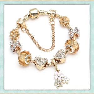 Macro shot of golden charm bracelet with heart, bow, and crystal pendants detail