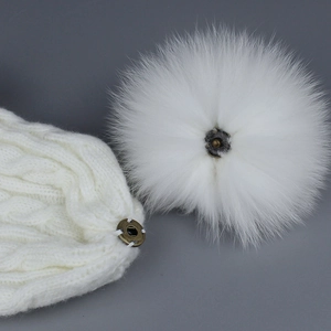 Bonnet en tricot blanc avec pompon en fourrure amovible montrant le bouton-pression en métal