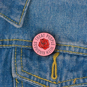 Detail of pink enamel rose brooch with Treat People With Kindness text on denim
