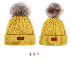 Détail du bonnet en maille jaune avec pompon amovible et étiquette en cuir