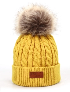 Détail du bonnet en tricot torsadé jaune pour enfant avec pompon et étiquette cuir