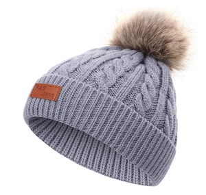 Détail d'un bonnet tricoté gris pour enfants avec pompon en fourrure et étiquette en cuir