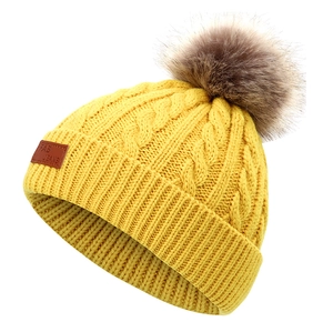 Détail d'un bonnet en tricot jaune vif avec pompon en fausse fourrure et étiquette cuir