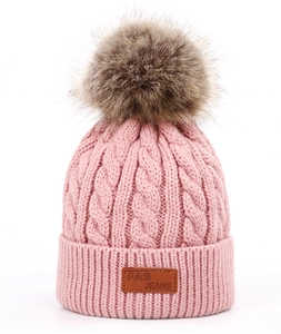 Détail d'un bonnet en maille rose avec des torsades et un pompon en fausse fourrure douce