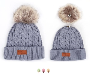 Détail de bonnets parent-enfant en maille torsadée grise avec pompons en fausse fourrure et cuir