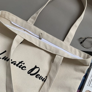 Detail of sturdy canvas tote bag featuring a secure top zipper and Lunatic Devil script