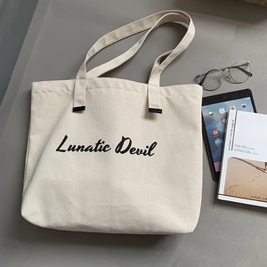 Detail of off-white canvas tote bag with Lunatic Devil print and lifestyle props