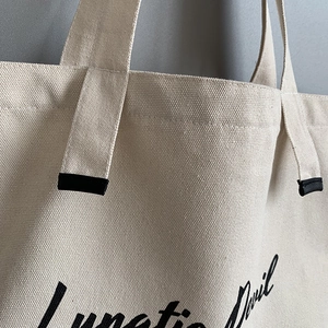 Detail of durable beige canvas tote bag showing handle stitching and Lunatic Devil text