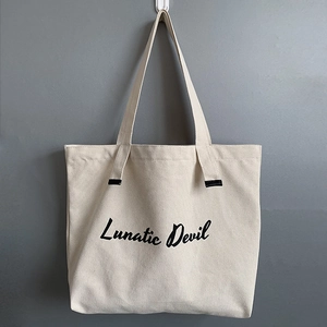 Close-up of cream canvas tote bag featuring black Lunatic Devil artistic printed lettering