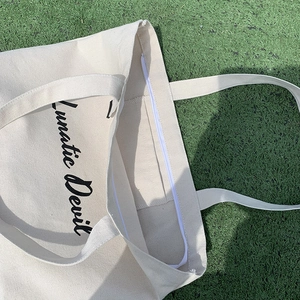 Detail view of cream canvas tote bag with black letter print and zipper inner pocket