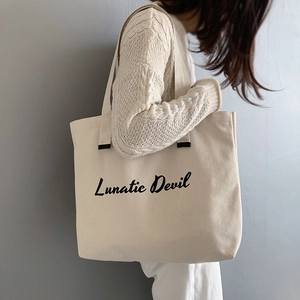 Side view of large off-white canvas tote bag with Lunatic Devil script on model