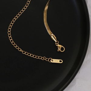 Macro detail of 14K gold snake chain necklace featuring lobster clasp and brand tag