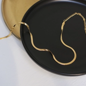 Close-up of golden flat herringbone snake chain necklace with metallic shine and extender