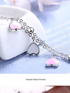Macro shot of silver chain with pink enamel heart pendant on white ceramic plate
