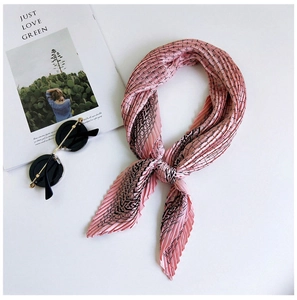Detail of pink pleated silk scarf with wavy patterns next to sunglasses and magazine
