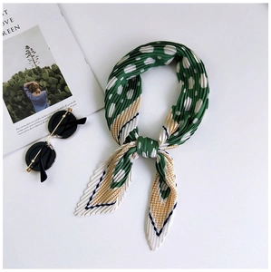 Detail of green and white polka dot pleated scarf styled in a knotted ring on white table