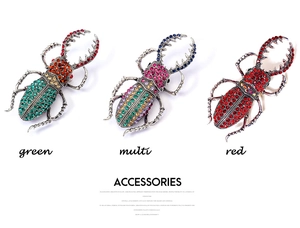 Détail de trois broches scarabées en strass rouges, verts et multicolores sur blanc