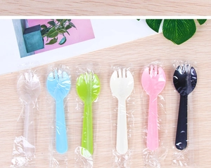 Close-up of individually wrapped disposable plastic sporks in assorted colors on wood table
