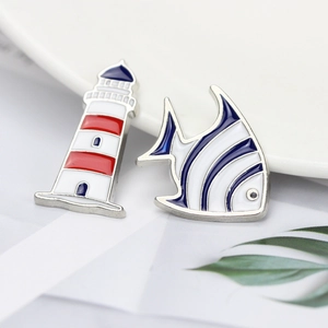 Cartoon enamel pins featuring a nautical lighthouse and tropical fish in silver metal