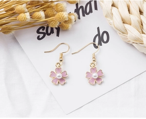 Detailed shot of pink enamel flower earrings with central pearl on soft textured background