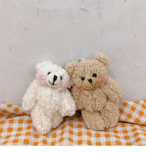 Detail of cream and khaki curly plush bear charms on a checkered fabric background