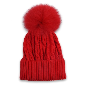 Detail of red cable-knit winter hat featuring a large fluffy faux fur pom-pom on top