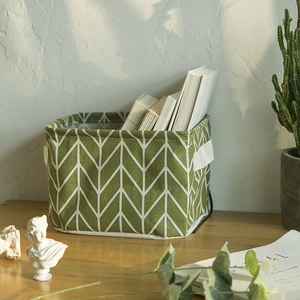 Green wave pattern foldable cotton linen storage basket on a minimalist wooden desktop