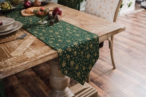 Macro detail of dark green Christmas table runner with golden snowflakes and elk patterns