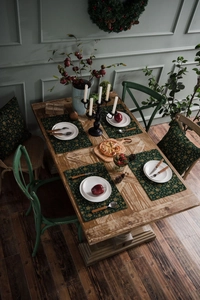 Close-up of four dark green cotton placemats with gold festive patterns on wood
