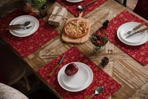 Detail of red Christmas placemats with gold reindeer and snowflake patterns on a wooden table