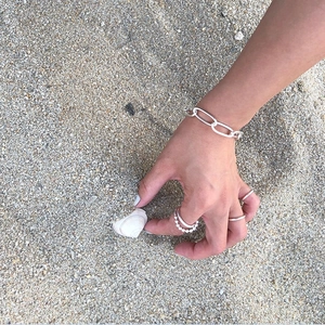 Detail shot of silver bead rings and thick chain bracelet on a beach with shells