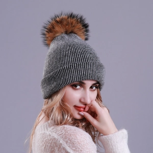Detail of grey knitted beanie featuring a fluffy faux fur pom-pom and ribbed texture