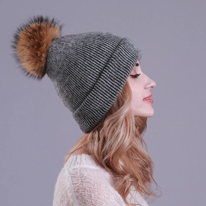 Close-up of a grey ribbed knit hat with a large faux fur pompom on a model