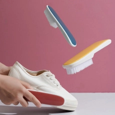 Aktion zum Reinigen weißer Sneaker mit bunten Kunststoffbürsten auf rosa Hintergrund