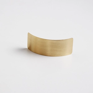 Close-up of a curved metal hair clip with a premium brushed gold finish and minimalist texture