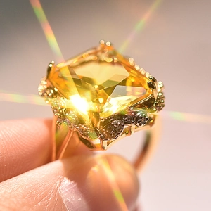 Macro shot of gold-plated ring with large square yellow stone and starburst light effect